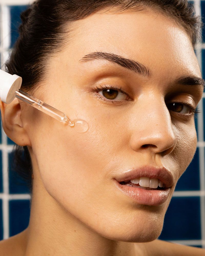 Nahaufnahme einer Frau, die Serum mit einer Pipette auf die Haut aufträgt. Gesicht und Pipette sind im Fokus.