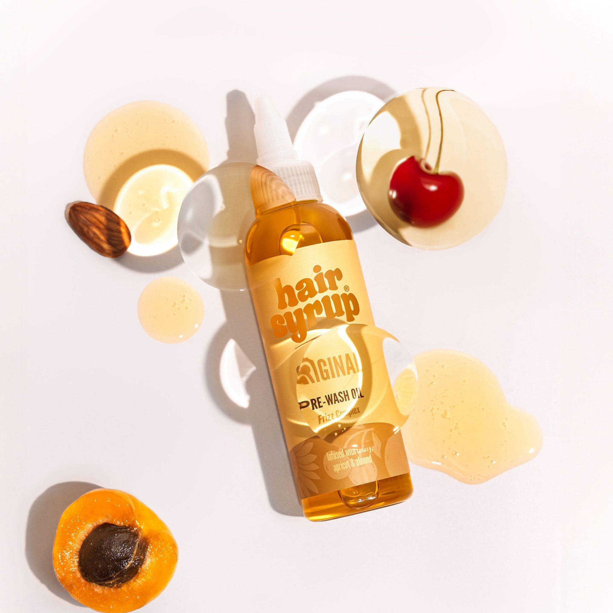 Flüssigkeit mit Produktetikett, Kirsche, Aprikose und Mandel auf hellem Hintergrund. Produktname: Hair Syrup The Original.
