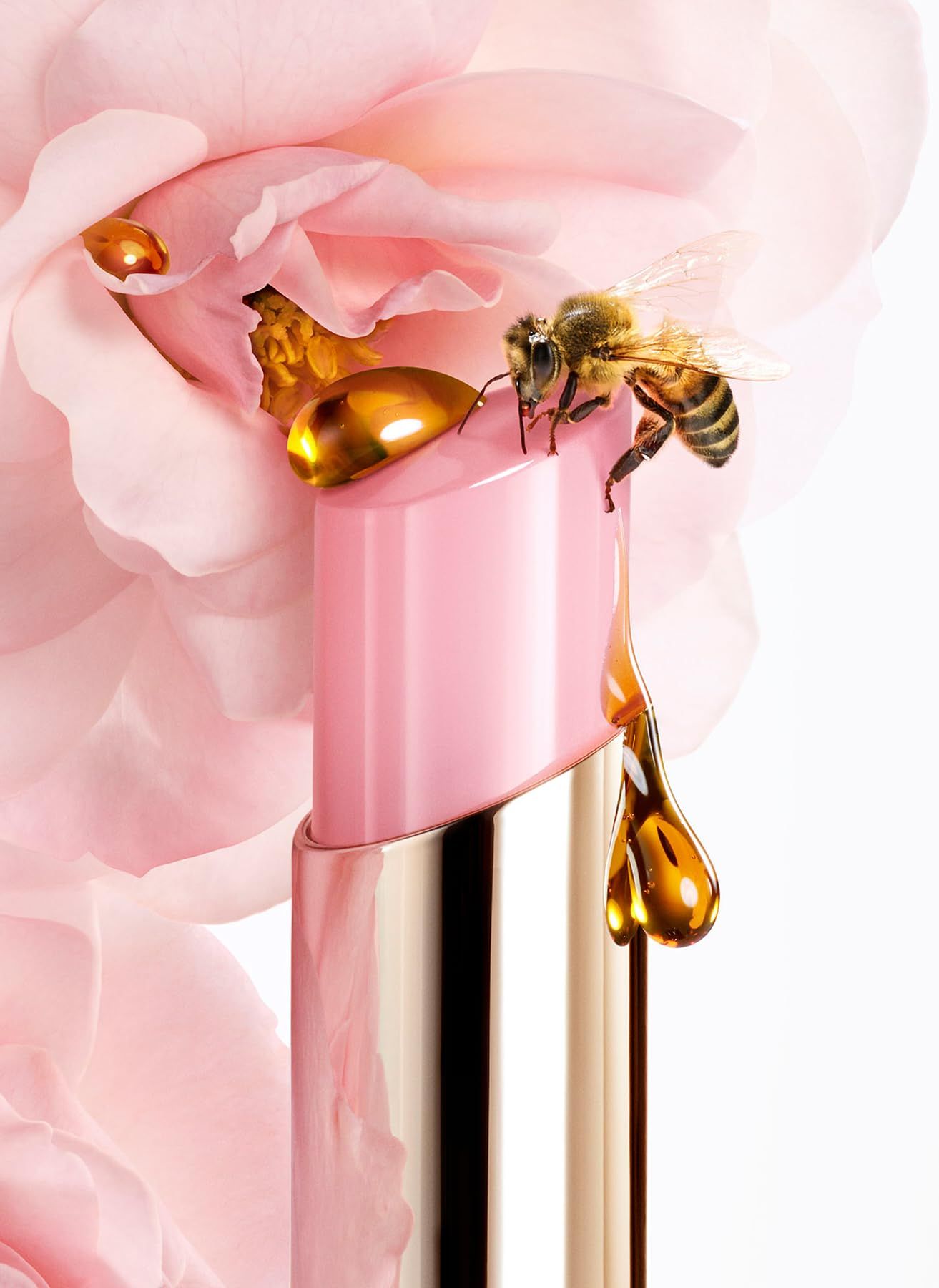 Ein Lippenbalsam mit rosa Hülle, goldfarbenen Details und einem Tropfen Honig, mit einer Biene.