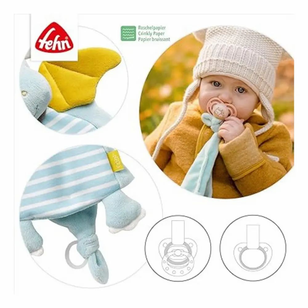 Baby mit Schnuller und Stoffdrachen. Marke: Fehn. Auf dem Drachen: Raschelpapier. Zeichnungen von Schnullern.