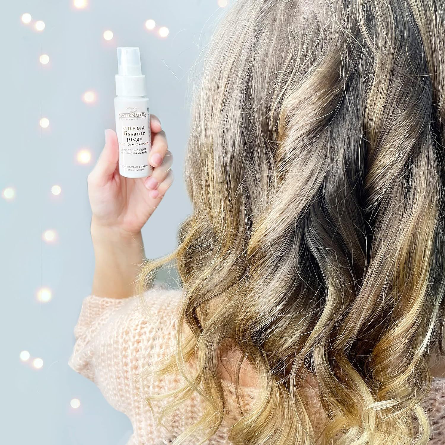 Frau hält eine kleine weiße Flasche mit Pumpspender vor ihr blondes Haar.