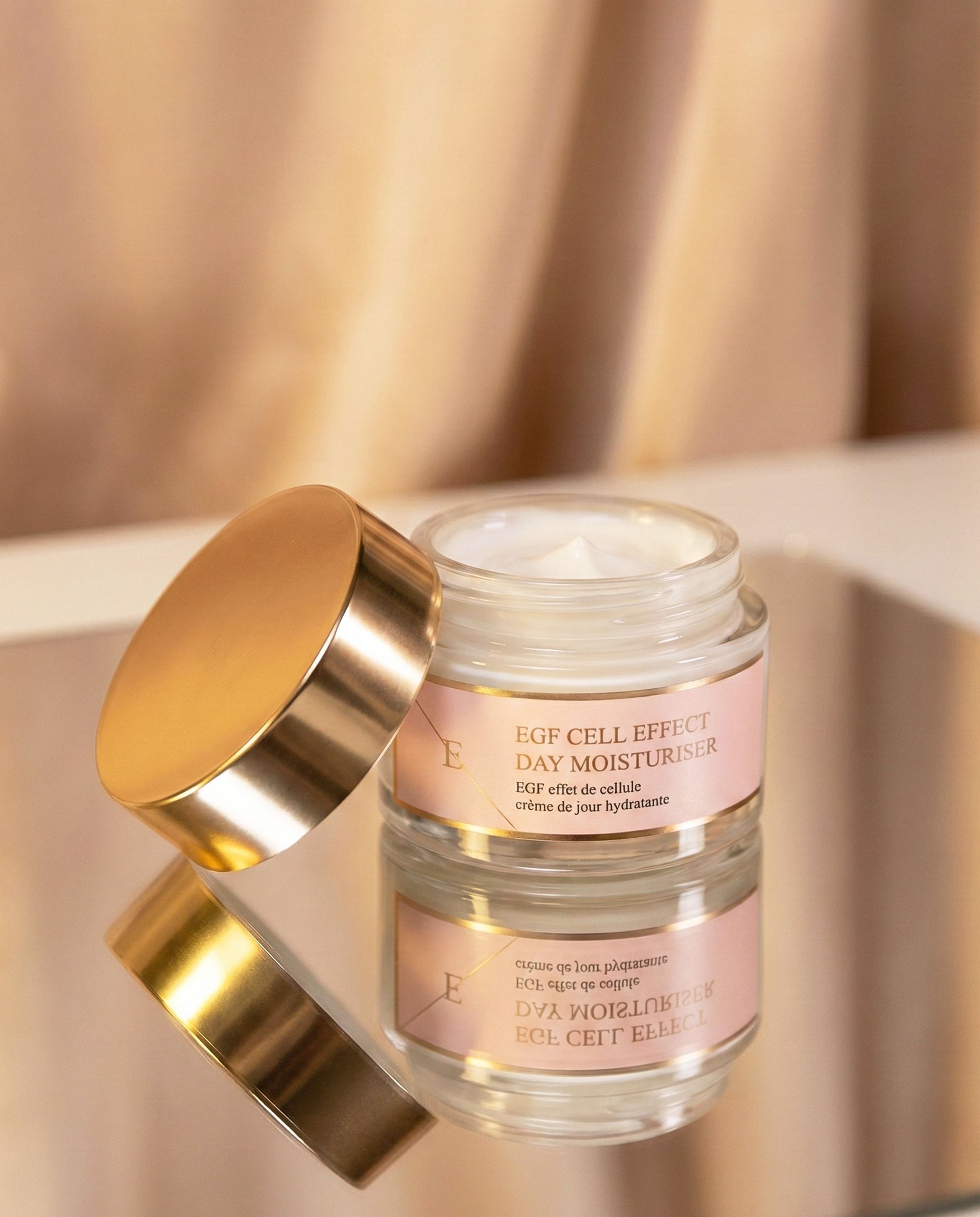 Offener Glascremetiegel mit goldenem Deckel, gefüllt mit weißer Creme, auf Spiegel.