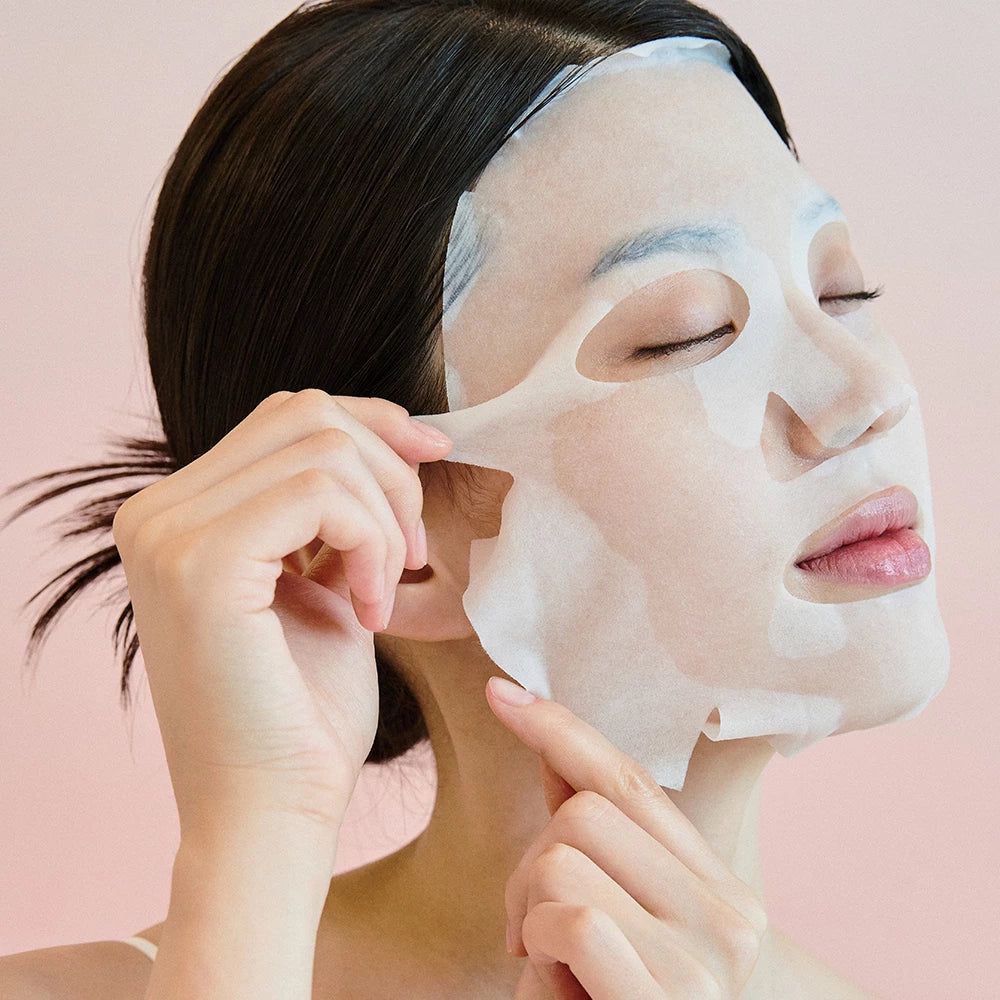 Frau trägt Gesichtsmaske. Hände ziehen Maske vom Gesicht. Rosa Hintergrund.