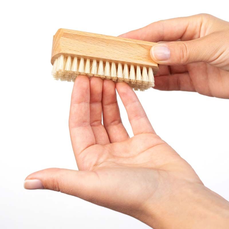 Hände halten Hand- und Nagelbürste aus Holz mit Naturborsten. Bürste wird über der Handfläche gehalten, Nahaufnahme.