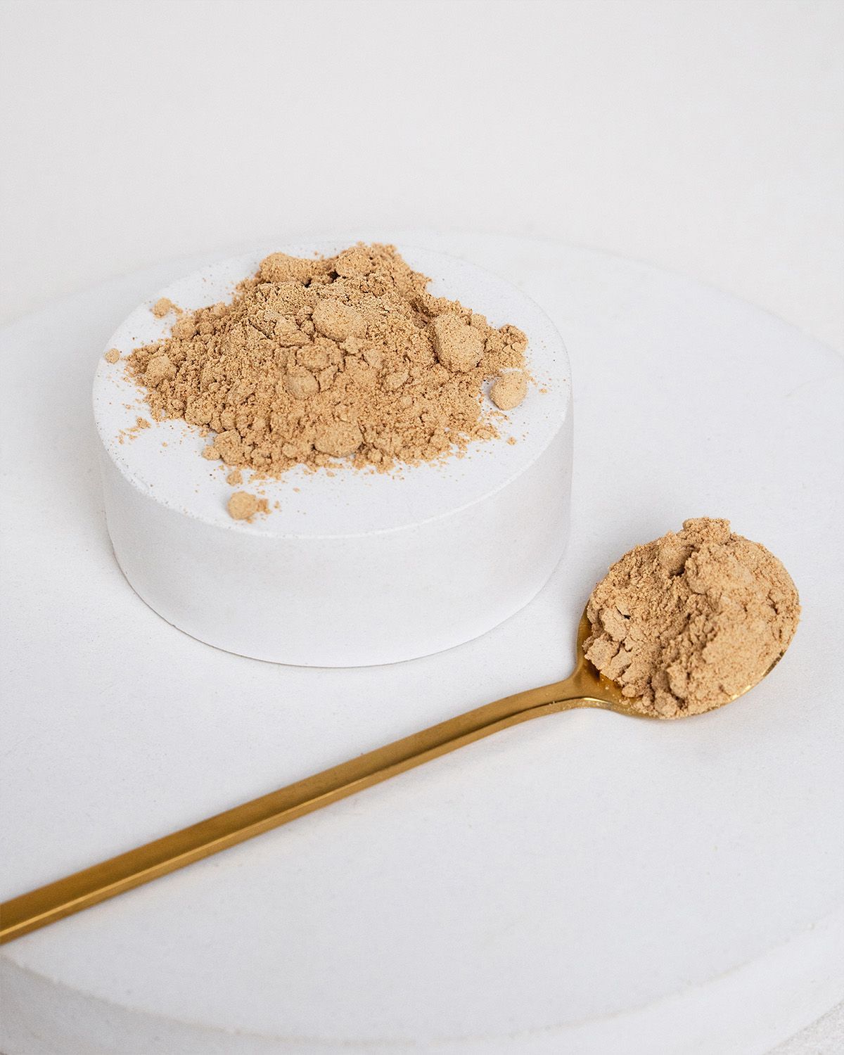 Braunes Maca-Pulver auf einem weißen Podest. Goldener Löffel daneben. Aufschrift: 100% BIO.
