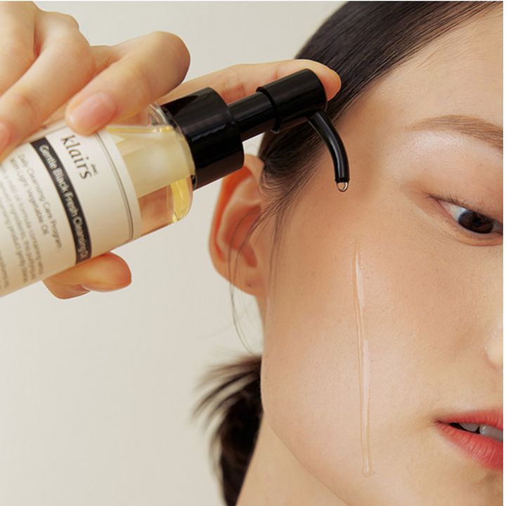 Eine Hand hält eine Flasche Gentle Black Fresh Cleansing Oil. Öl wird auf die Haut aufgetragen.