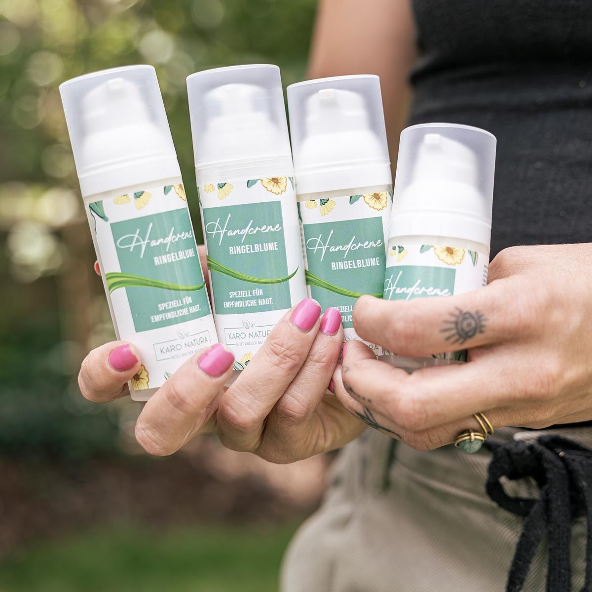 Vier Handcreme-Spender mit floralem Etikett. Aufschrift: Handcreme Ringelblume, Karo Natura. In einer Hand gehalten.
