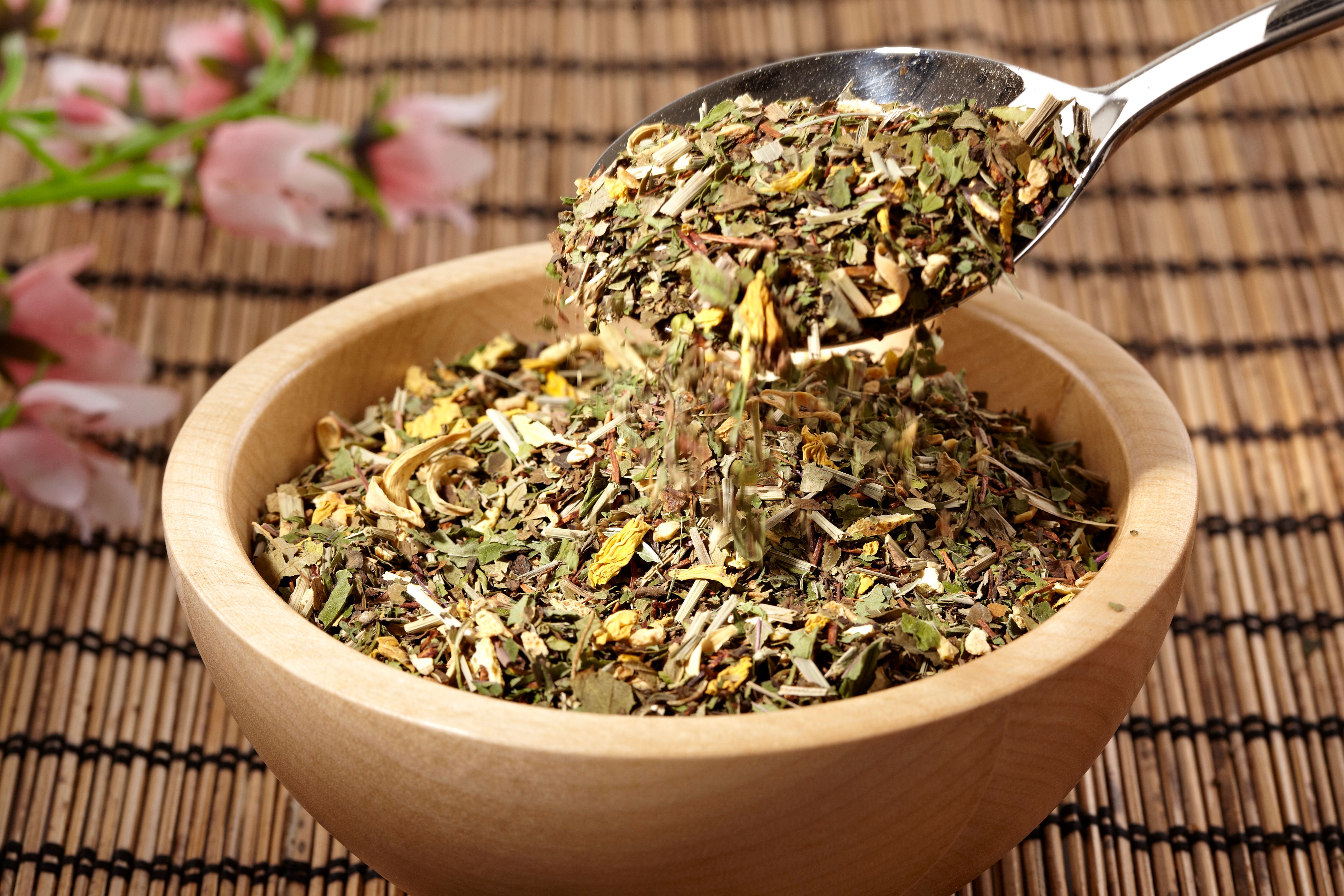Holzschale gefüllt mit Kräutermischung. Ein Löffel hebt Kräuter aus der Schale.
