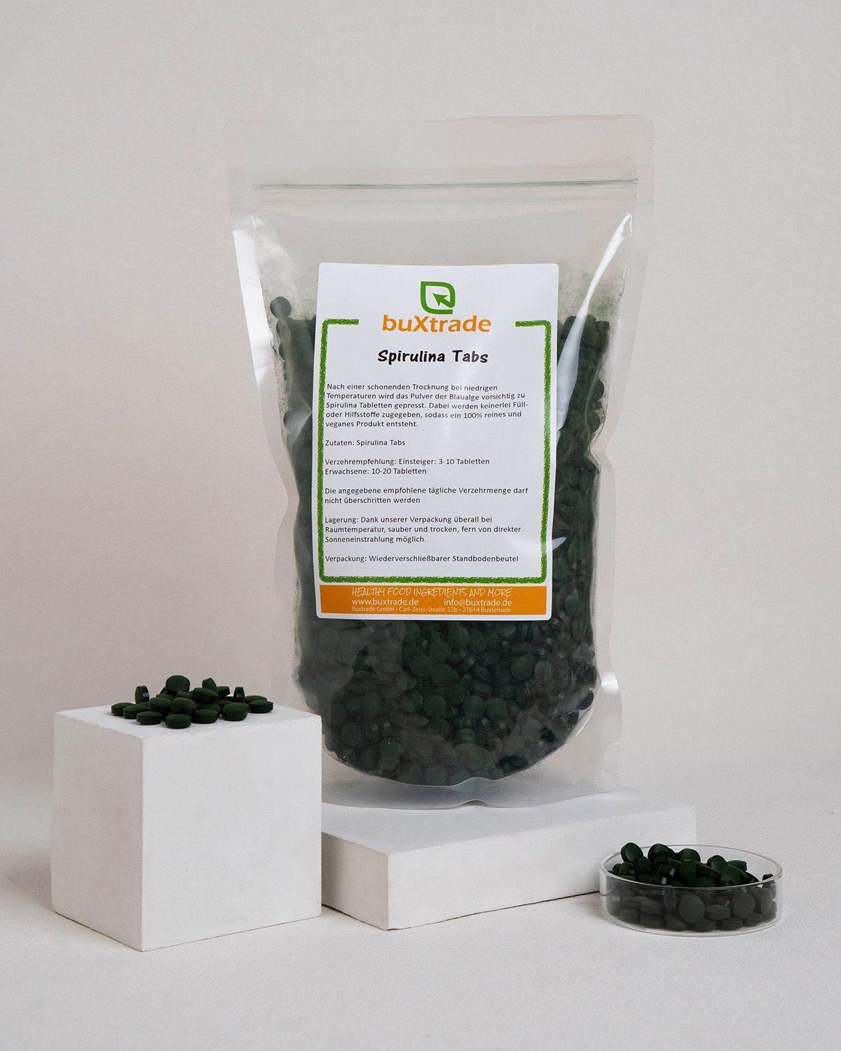 Beutel mit Tabletten, daneben Schale und Tabletten auf Block. Produktname und Informationen auf dem Etikett.