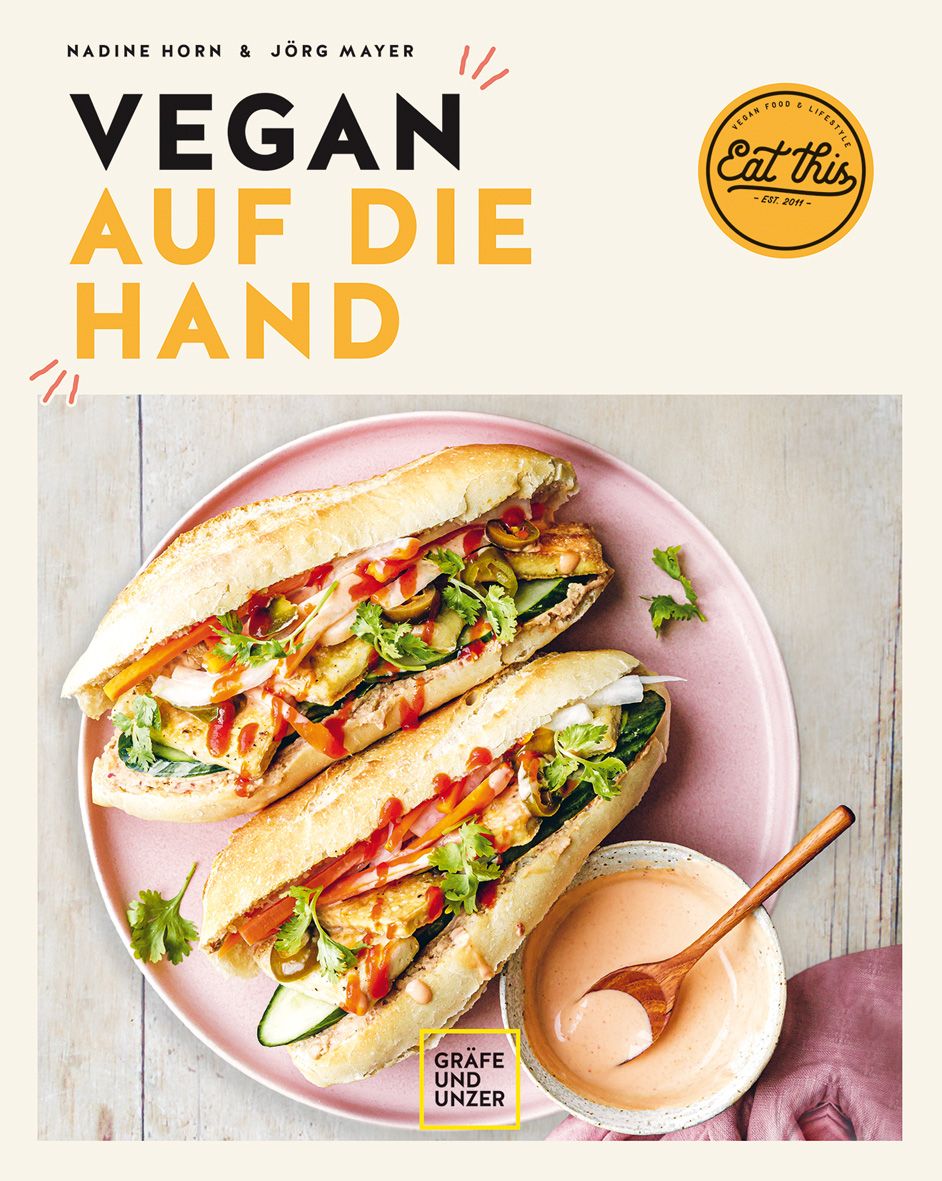 Buchcover mit dem Titel "Vegan auf die Hand". Zwei gefüllte Baguettes auf einem rosa Teller, daneben eine Schüssel mit Sauce.