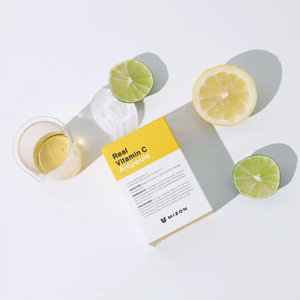 Verpackung mit gelbem Etikett und Aufschrift: Real Vitamin C Ampoule. Zitronen, Limetten und ein Becher daneben.