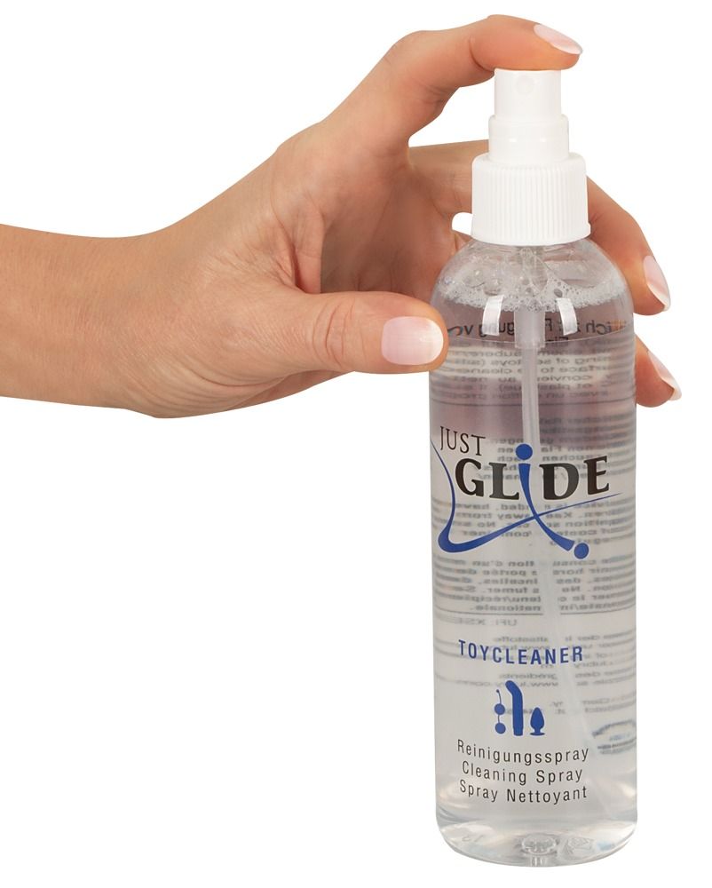 Klare Sprühflasche mit weißem Sprühkopf. Aufschrift "JUST GLIDE TOYCLEANER". Hand hält die Flasche.