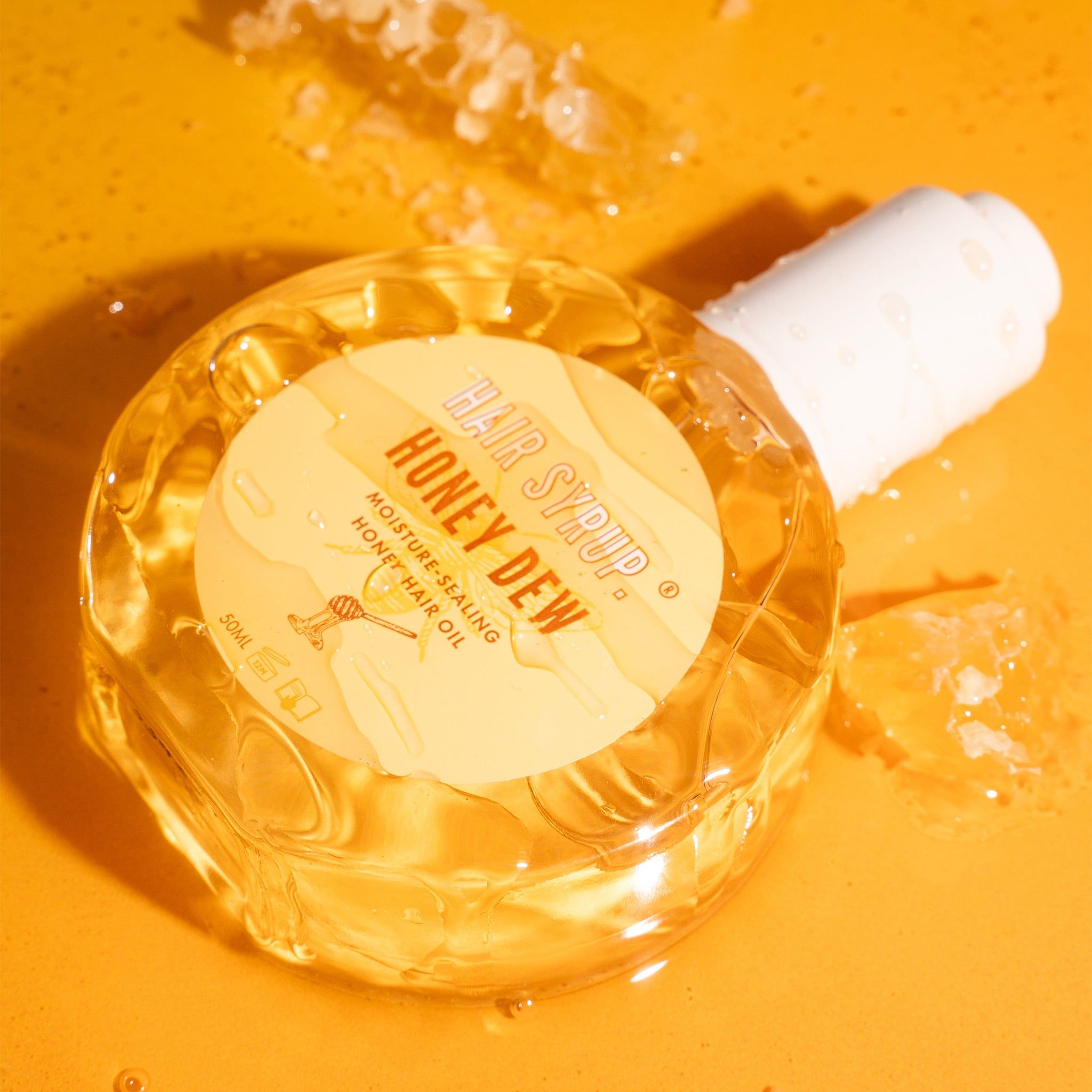 Runde Glasflasche mit weißem Deckel. Aufkleber mit Text. Flasche liegt auf gelbem Untergrund. Honigwaben im Hintergrund.