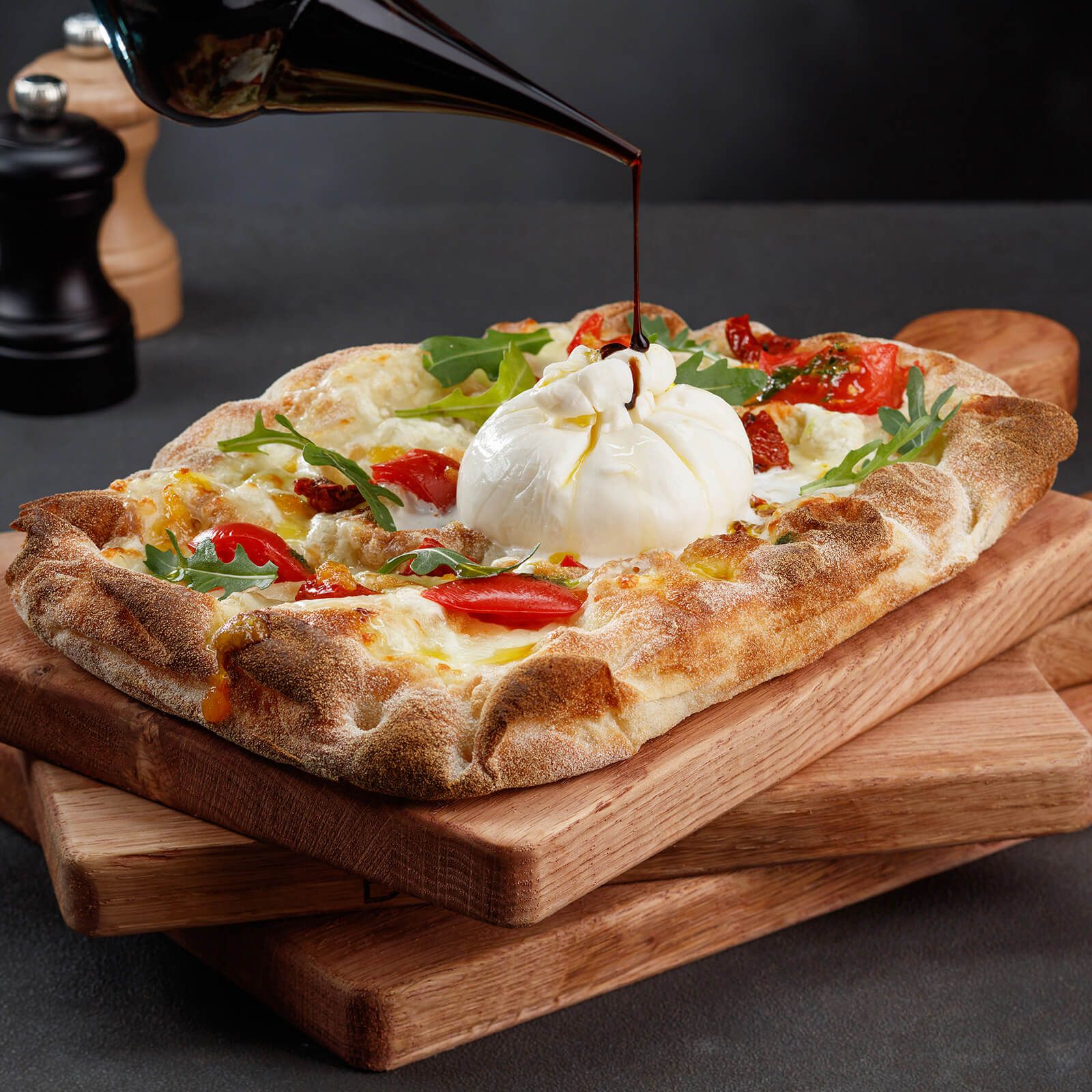 Rechteckiger Pizzaboden mit Burrata, Tomaten und Rucola, beträufelt mit Balsamico.