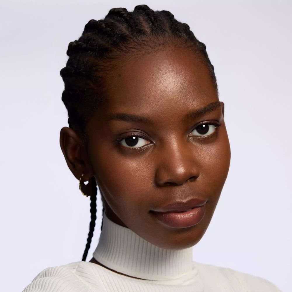 Porträt einer Frau mit dunkler Haut und geflochtenen Haaren. Sie trägt einen weißen Rollkragen.