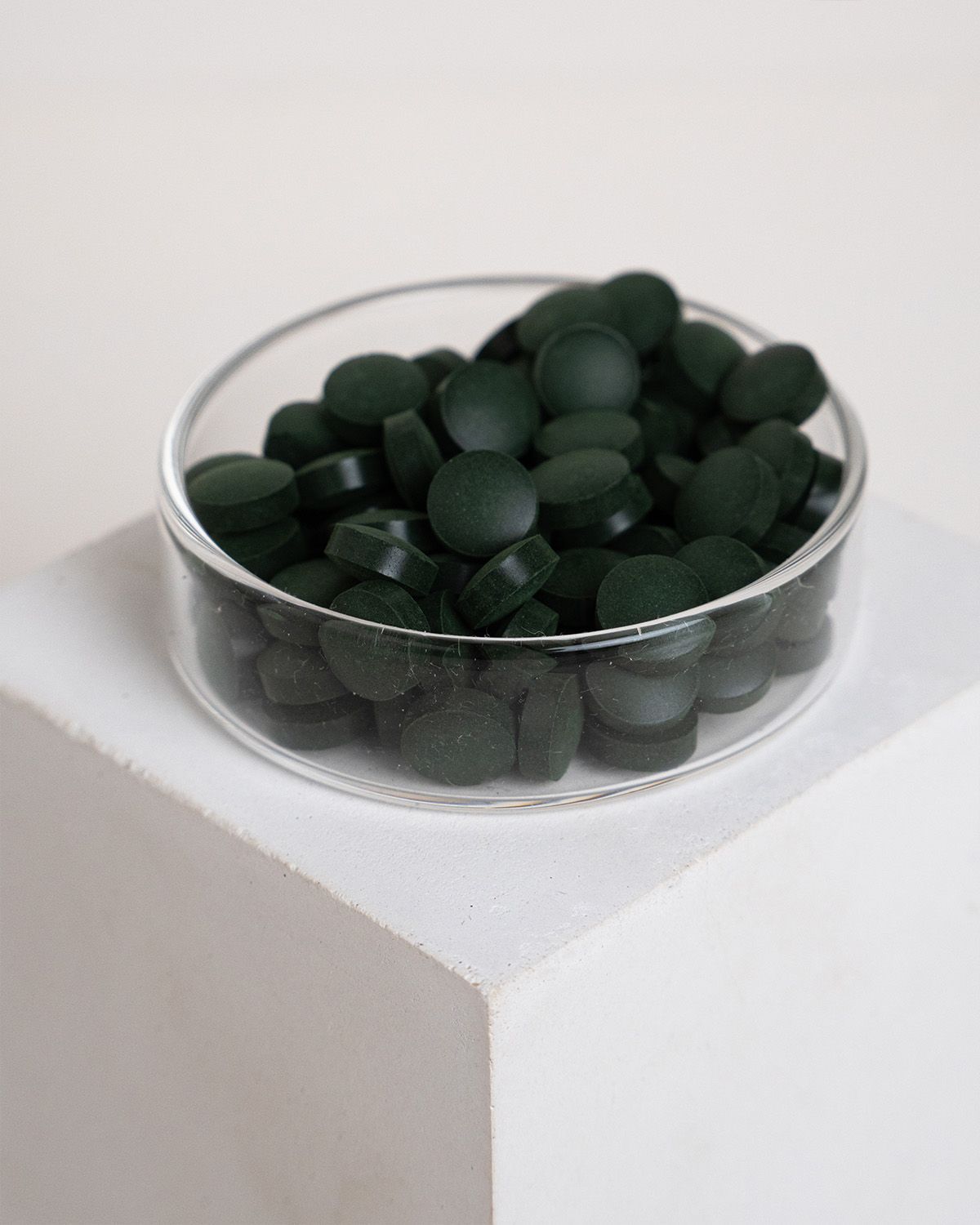 Eine Glasschale mit grünen, runden Tabletten. Die Tabletten sind flach und haben eine dunkle Farbe.