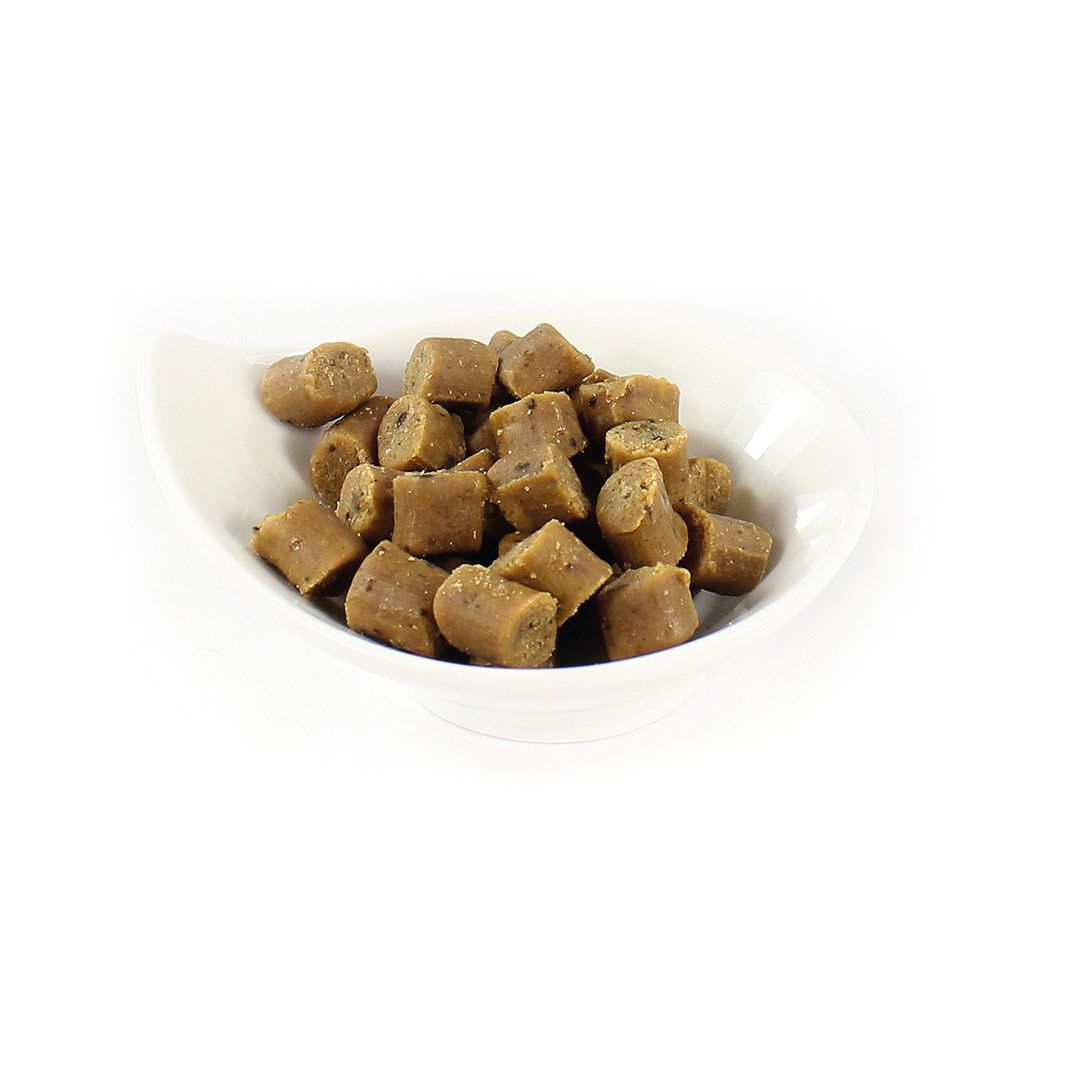 Hundesnack in einer weißen Schale. Kleine, braune, würfelförmige Stücke mit dunklen Punkten.