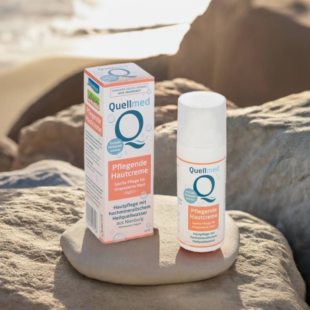 Creme-Tube und Box von Quellmed. Aufschrift: Pflegecreme. Box mit Logo und Text. Hintergrund: Stein und Wasser.