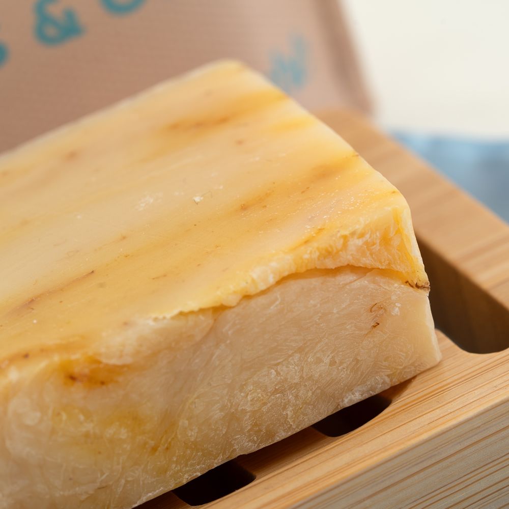 Rechteckige Seife "Lemongrass & Glow" auf Holzablage. Helle Farbe mit sichtbaren Texturen.