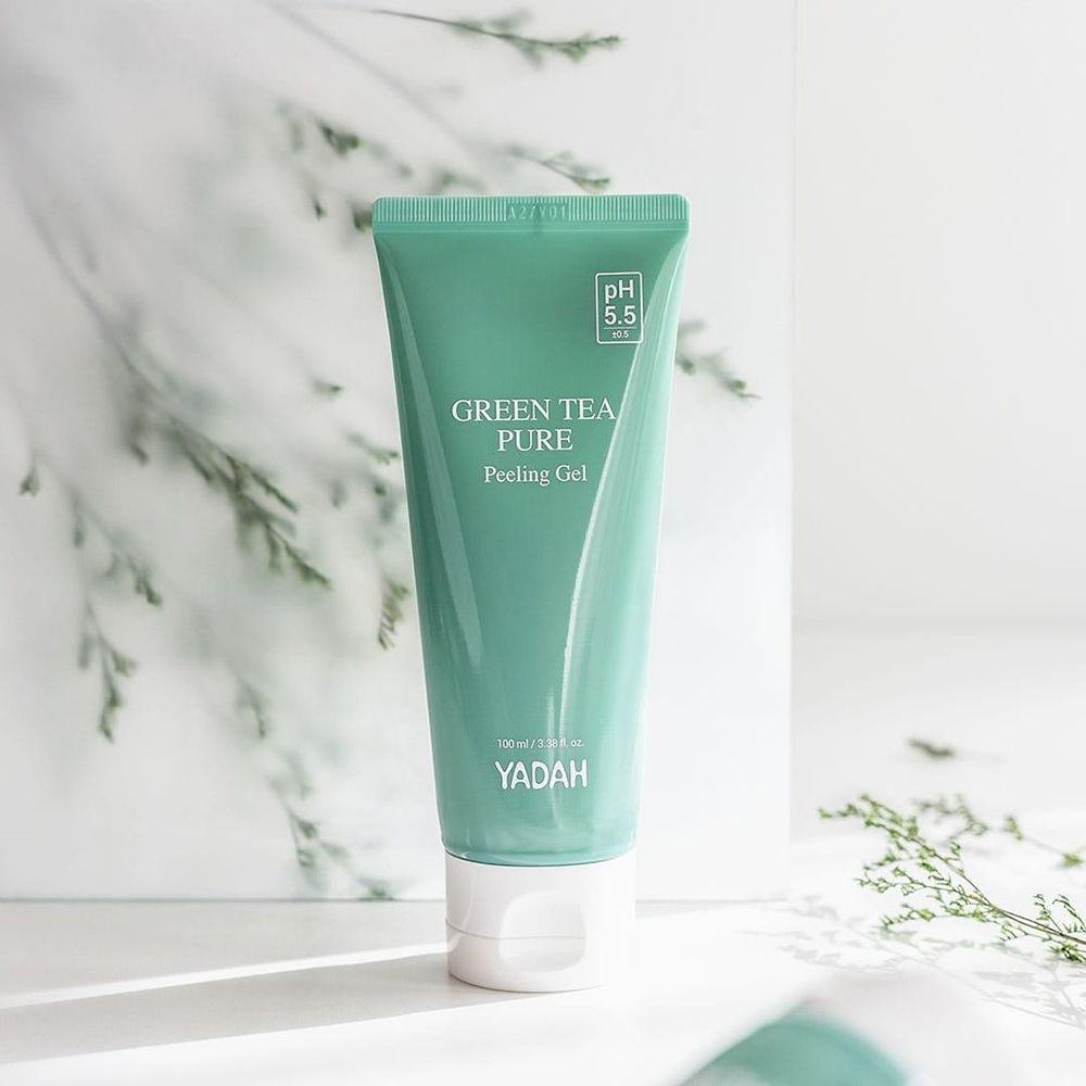 Grüne Tube mit weißem Verschluss. Aufschrift: Green Tea Pure Peeling Gel. Marke: Yadah. pH 5.5. Hintergrund mit Zweigen.