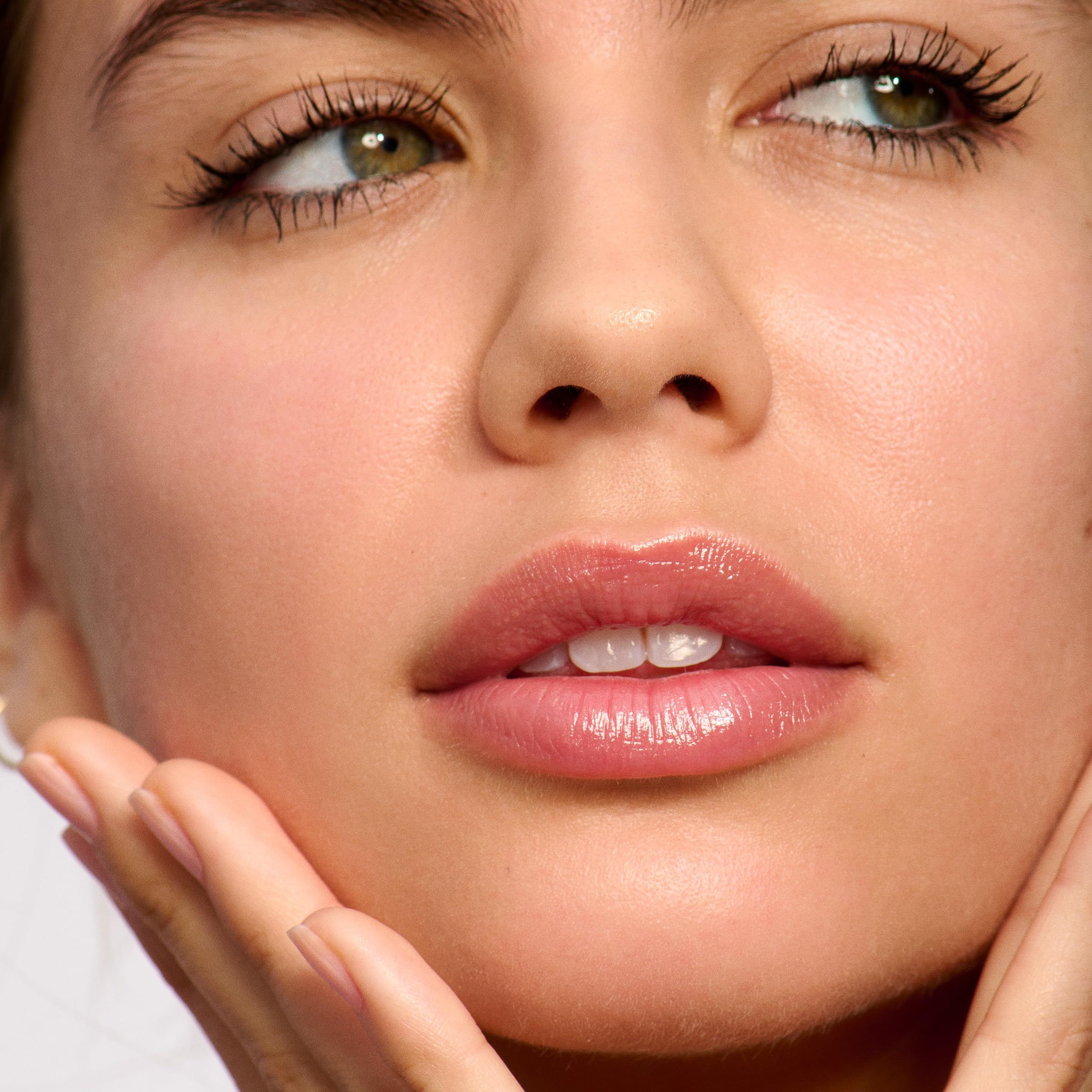 Nahaufnahme eines Gesichts mit glänzenden Lippen. Die Person berührt ihr Gesicht. Grüne Augen.