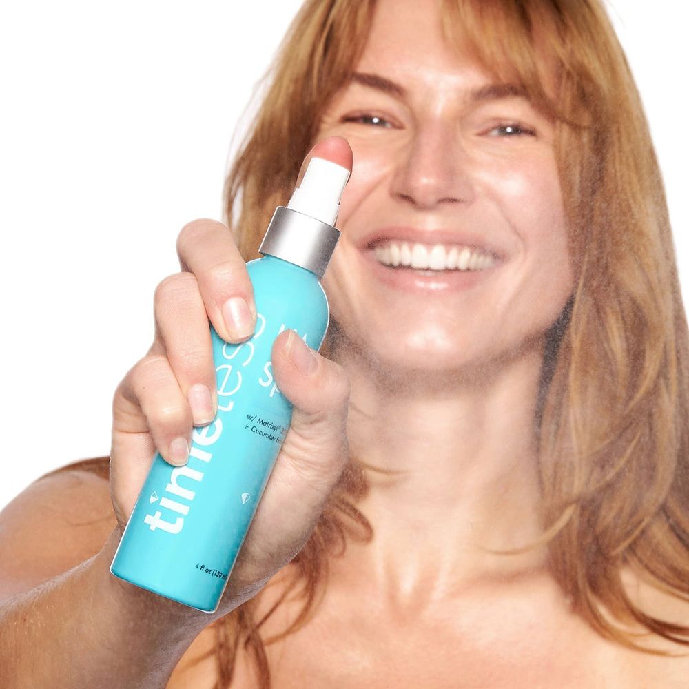 Frau sprüht mit türkisfarbener Flasche. Aufschrift: timeless HA Spray. Sprühkopf weiß. Gesicht der Frau. 