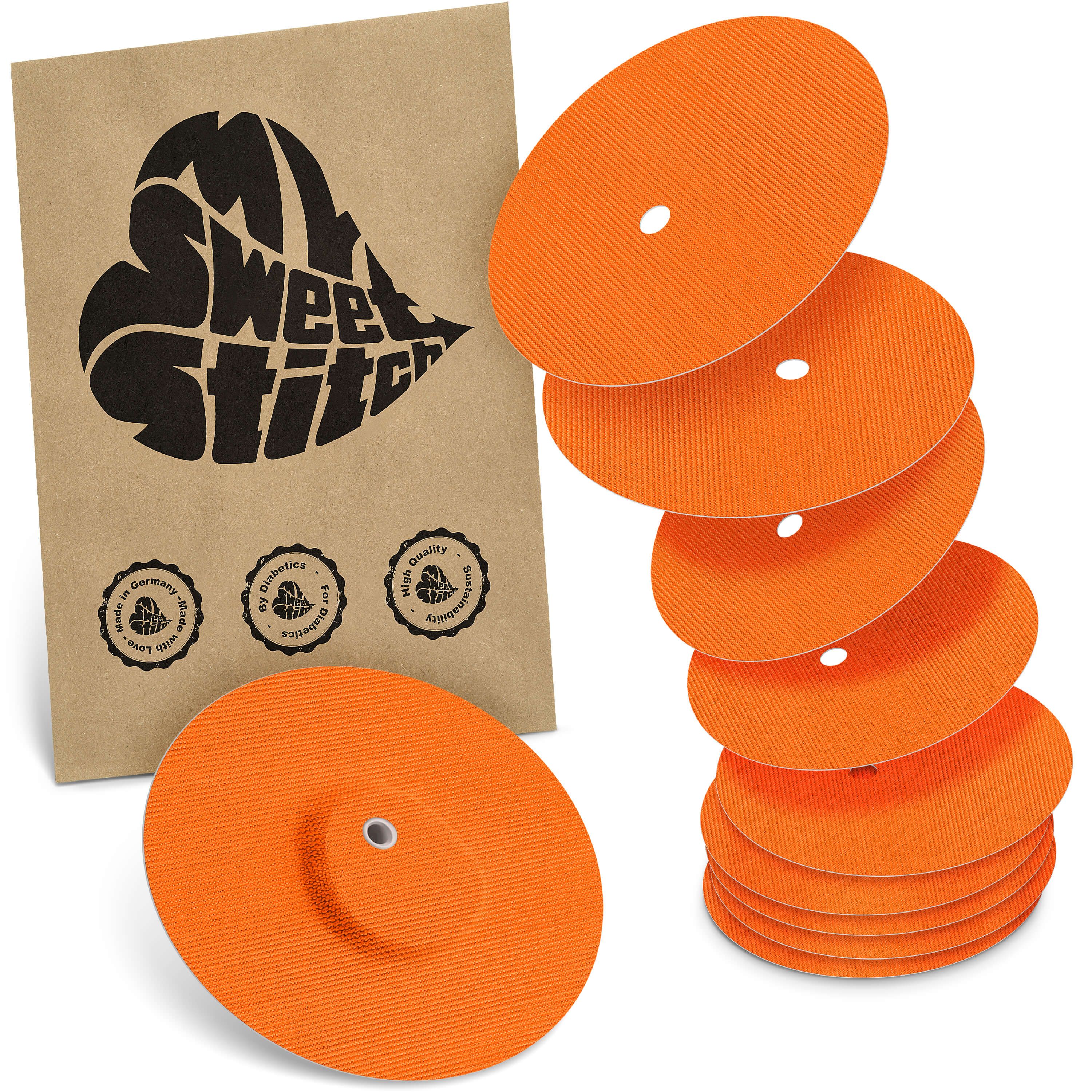 Ein Stapel oranger, runder Pads mit zentralem Loch, daneben ein einzelnes Pad und eine braune Papiertüte mit schwarzem Herz-Logo.