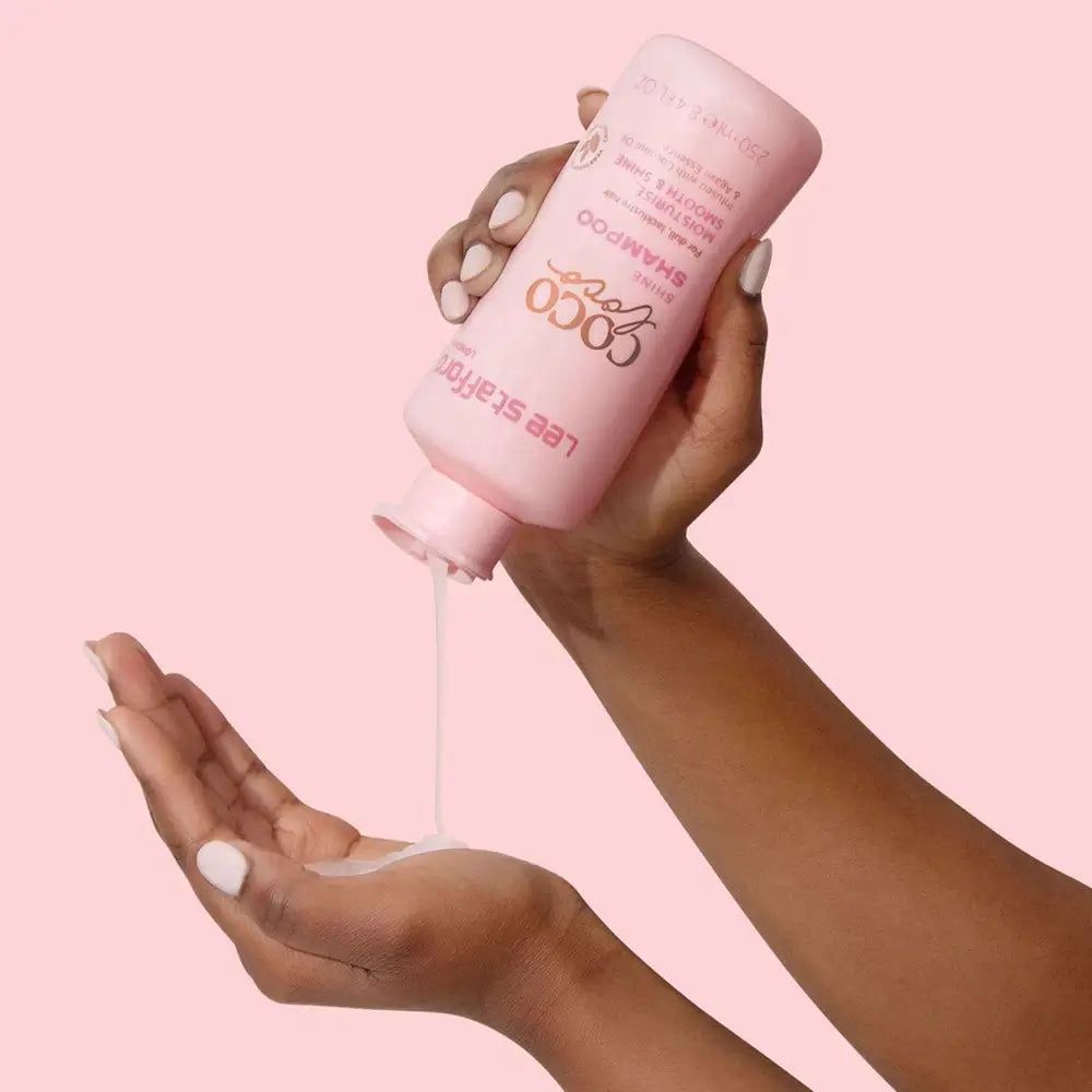 Hände halten eine rosa Flasche CoCo LoCo Shine Shampoo. Shampoo wird in die Hand gegossen. Vegan-Logo.