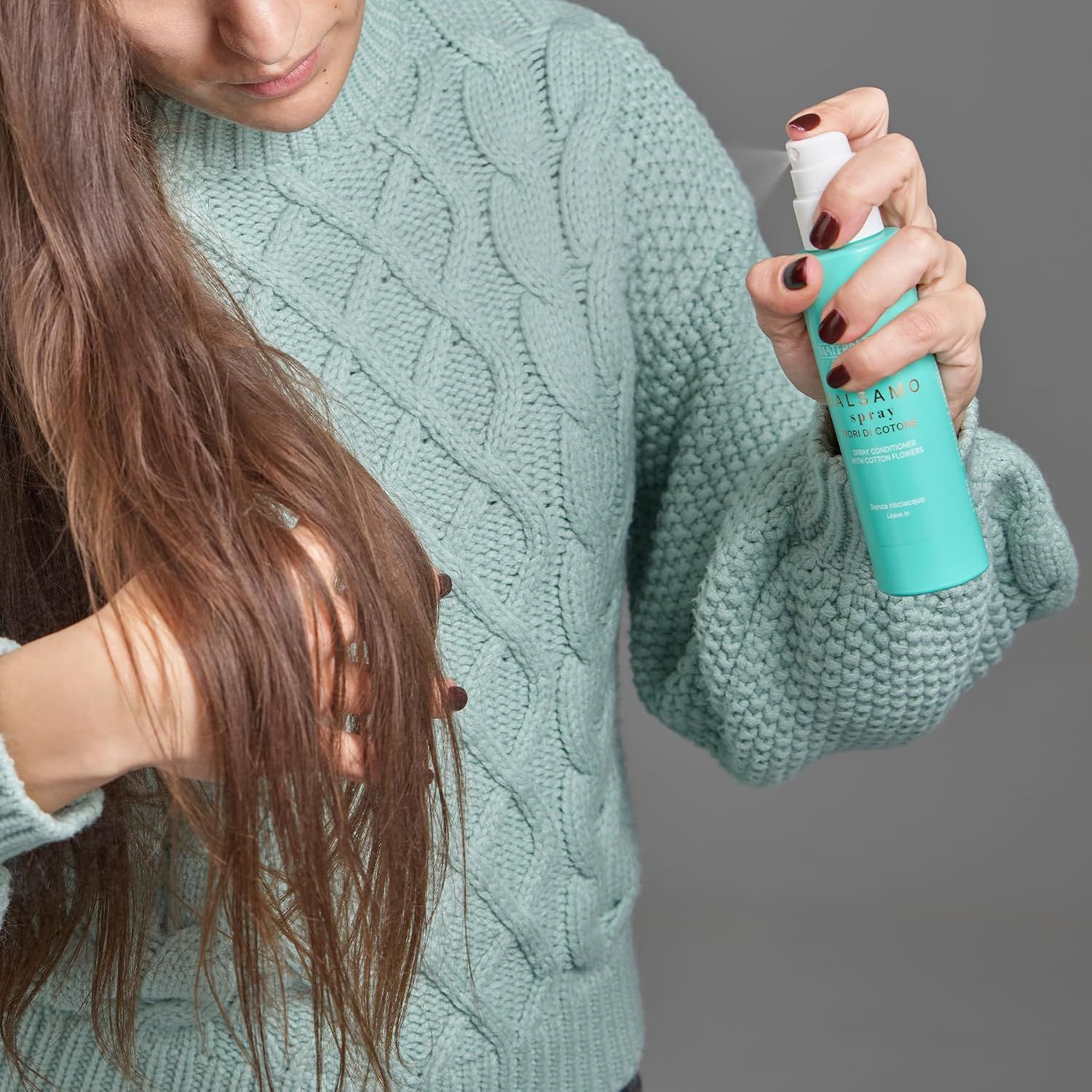 Frau mit langen Haaren sprüht ein Produkt auf ihr Haar.
