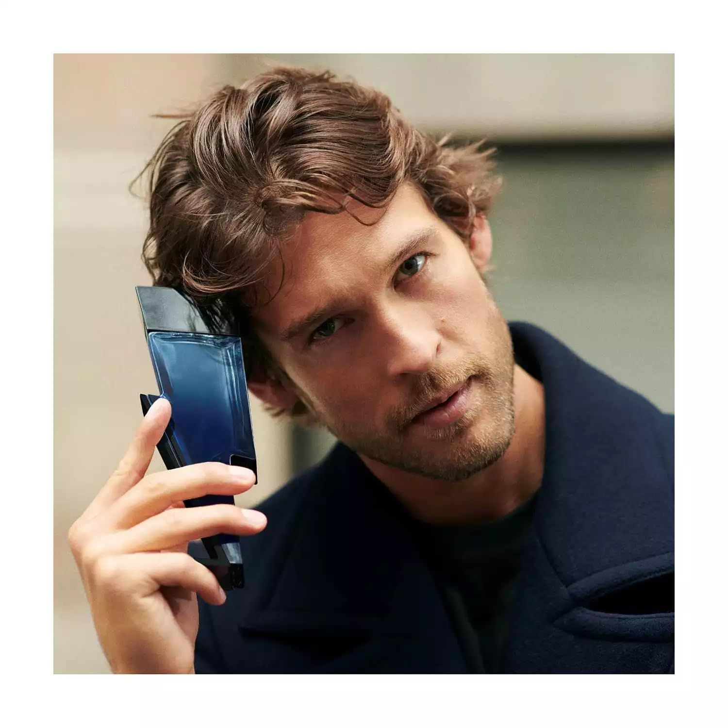 Mann hält blauen Flakon in Blitzform. Schwarzer Deckel. Mann trägt einen blauen Mantel. Blick in die Kamera.