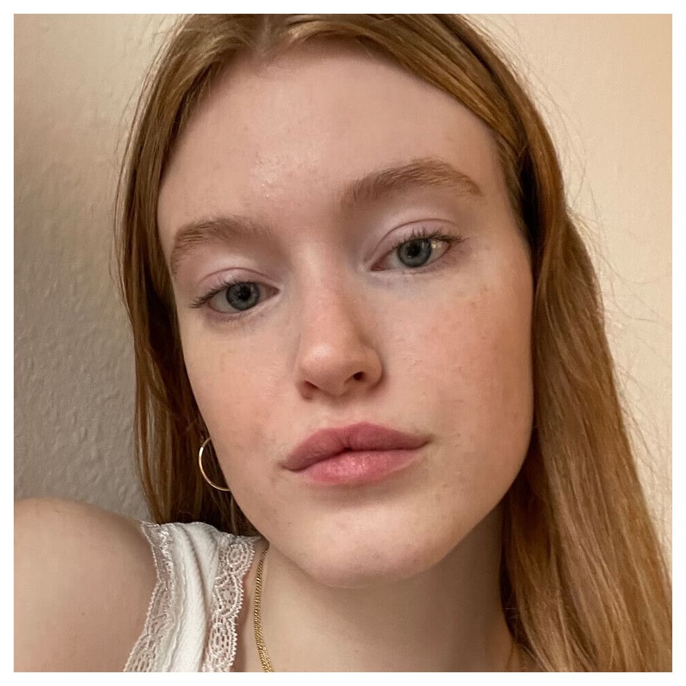 Nahaufnahme einer Frau mit heller Haut und Sommersprossen. Sie trägt ein weißes Top. Blick direkt in die Kamera.