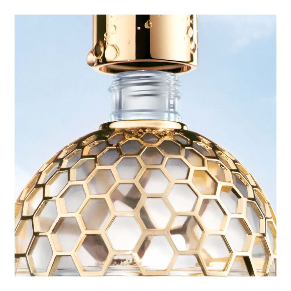 Parfümflasche mit goldfarbenem Wabenmuster-Dekor und goldfarbenem Verschluss. Detailaufnahme, blauer Hintergrund.