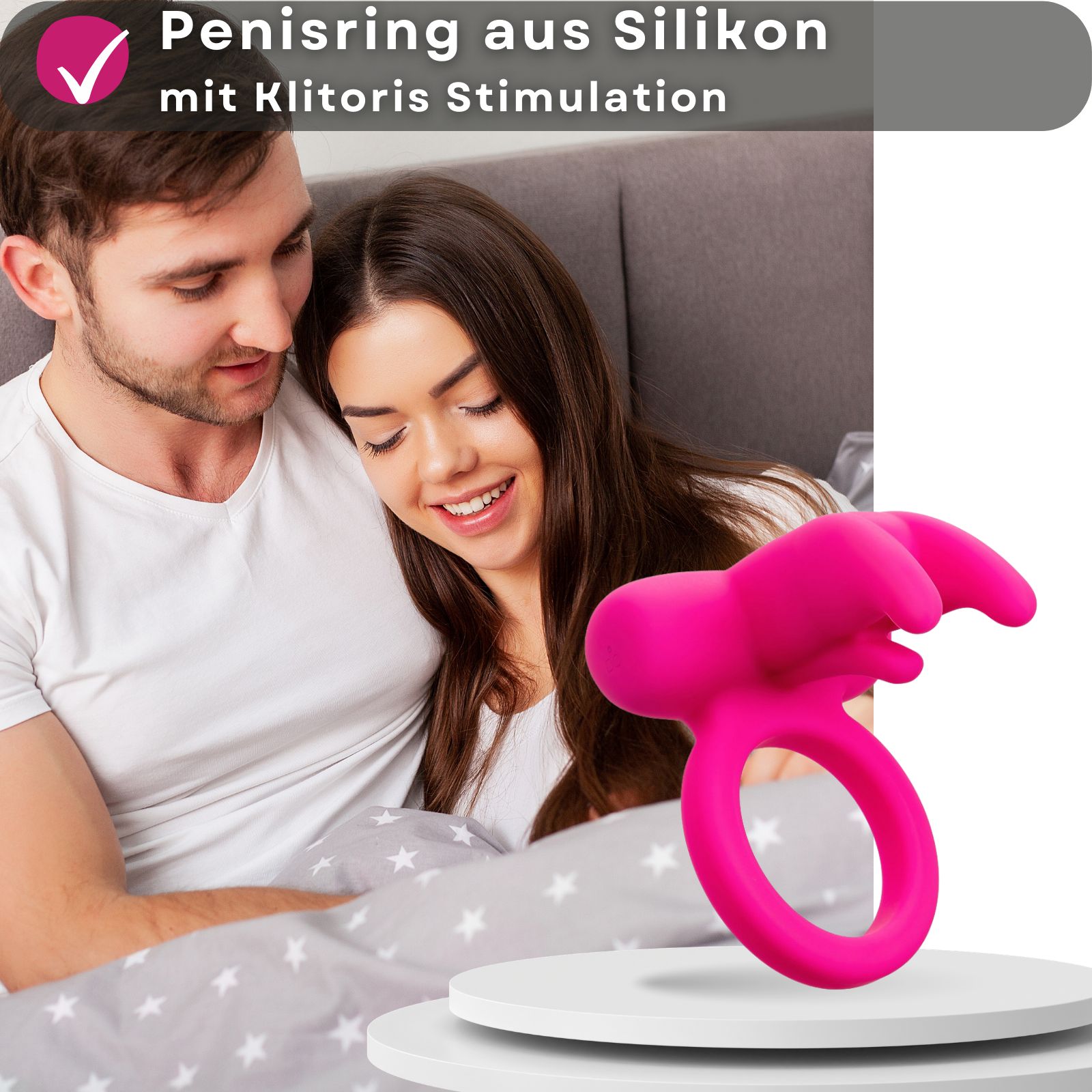 Pinkfarbener Penisring aus Silikon mit Klitoris Stimulation. Auf weißem Podest, Hintergrund: Paar.