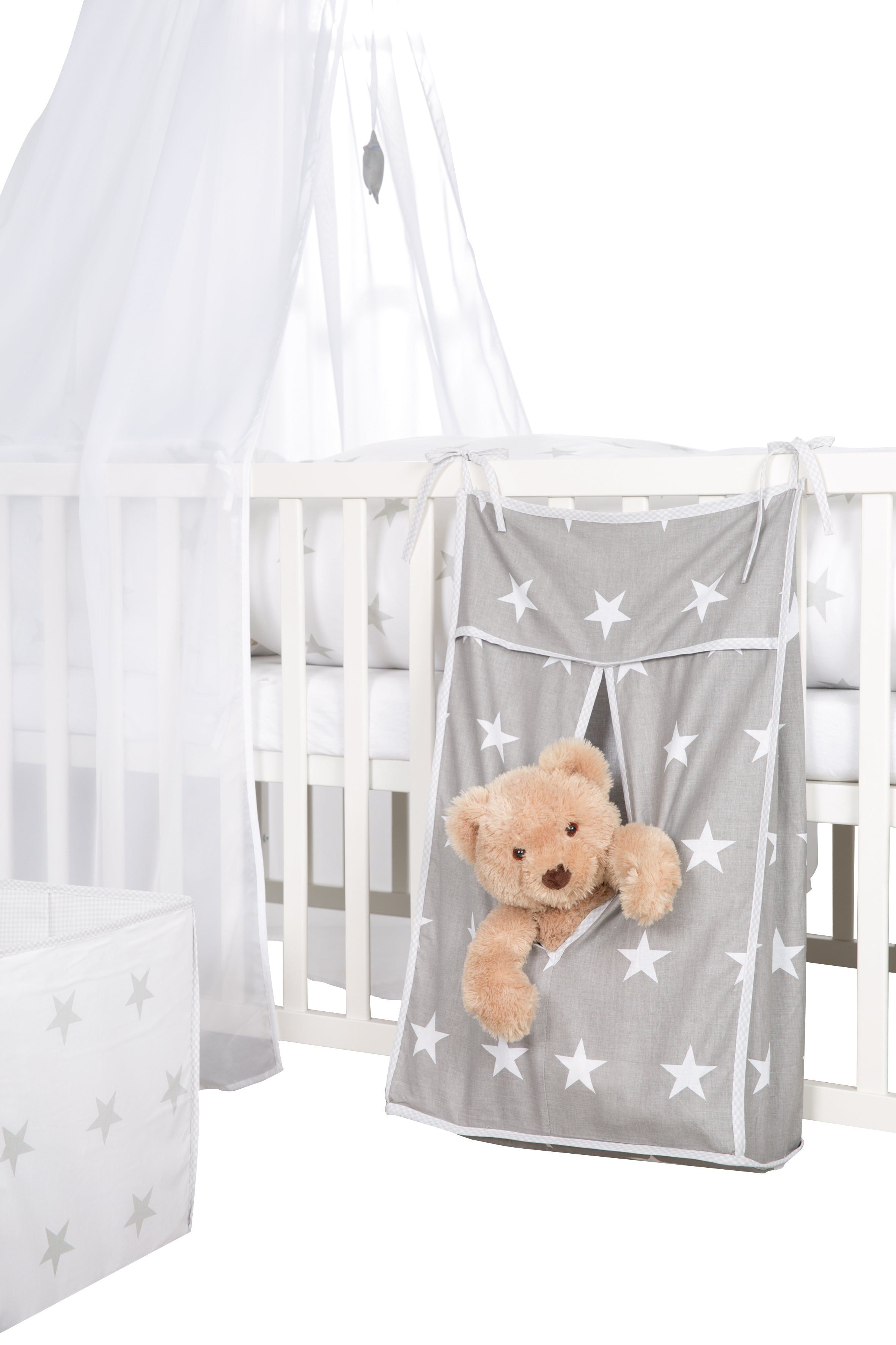 Grauer Stofforganizer mit Sternen an einem weißen Kinderbett. Ein Teddybär steckt in der offenen Tasche.