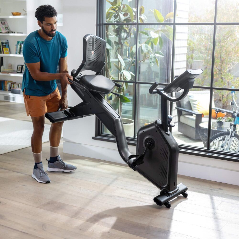 Mann justiert Heimtrainer. Schwarzes Gerät mit Display. Marke: Schwinn.