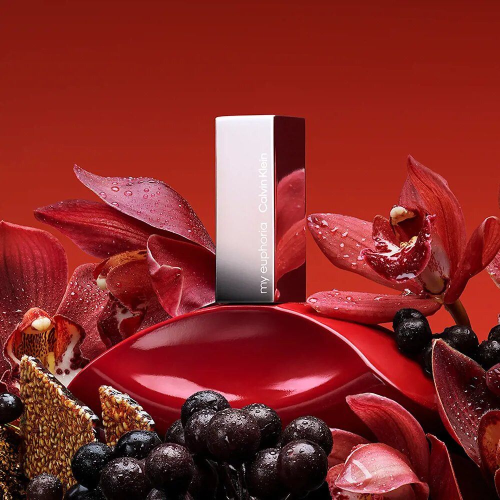 Roter Flakon mit silbernem Verschluss. Aufschrift: my euphoria Calvin Klein. Umgeben von roten Blüten.