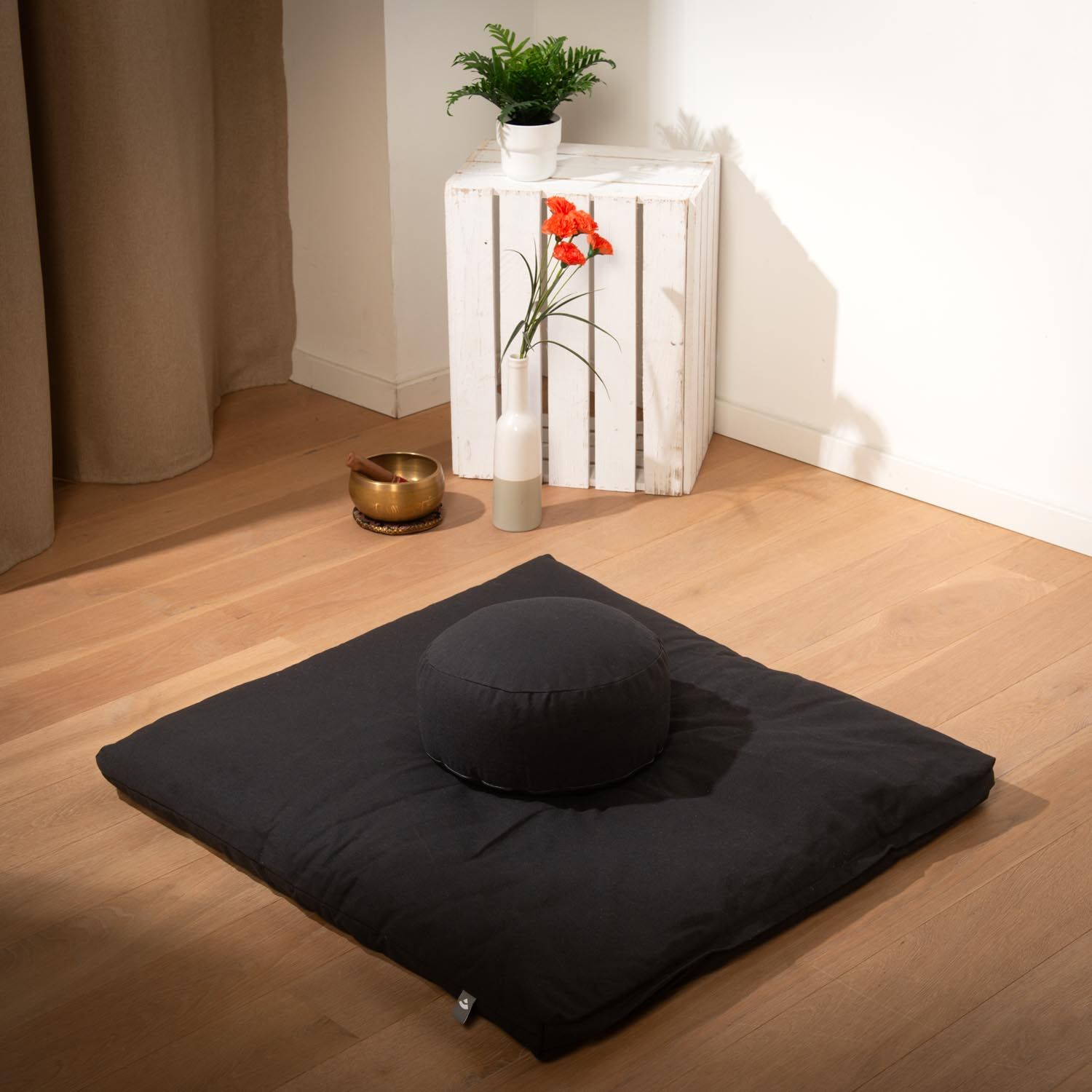 Schwarzes Meditationskissen und Matte auf Holzboden. Runde und quadratische Formen.