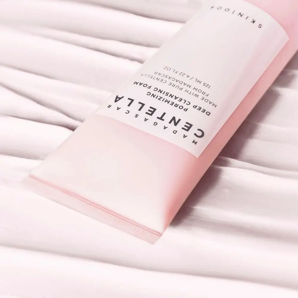 Nahaufnahme eines rosa Tubenabschnitts. Text: MADAGASCAR CENTELLA, Poremizing Deep Cleansing Foam. Marke SKIN1004.