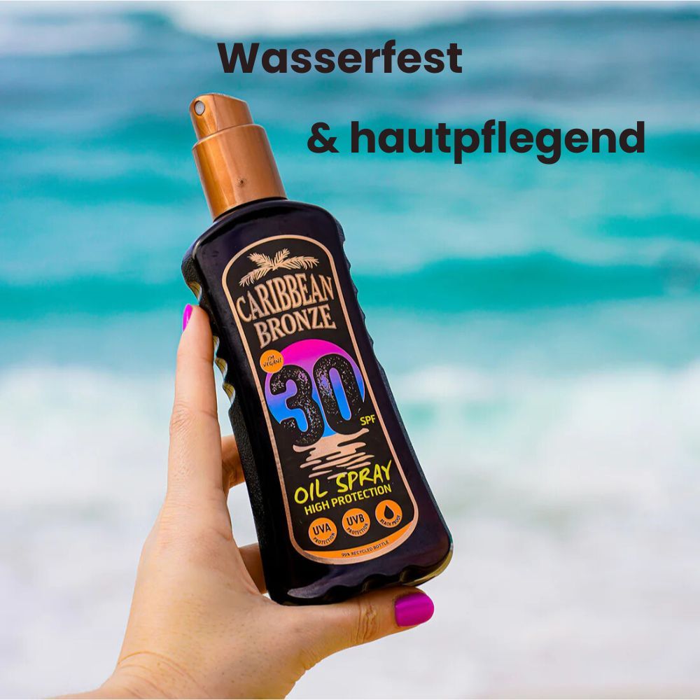 Hand hält eine braune Flasche mit Sprühkopf. Aufschrift: Caribbean Bronze, LSF 30, Oil Spray. UVA, UVB Schutz. Hintergrund: Meer.