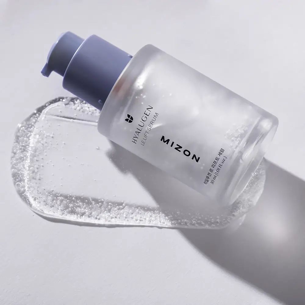 Serumflasche liegt auf einer Serumspur. Aufschrift: HYALUGEN LE LIFT SERUM, MIZON. Serumspur mit Blasen.