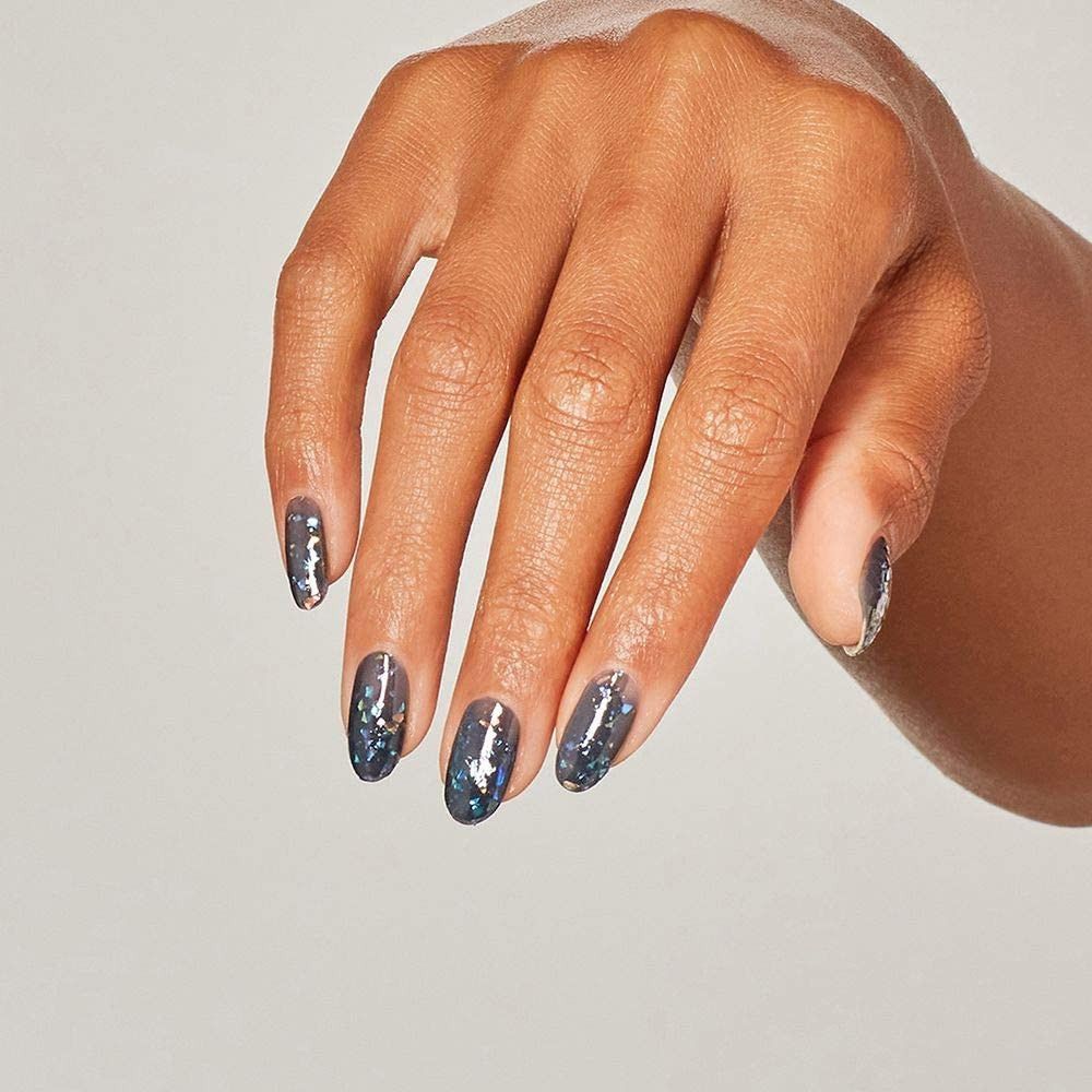Hand mit oval geformten Nägeln, lackiert mit schimmerndem Nagellack. Helle Haut, neutraler Hintergrund.