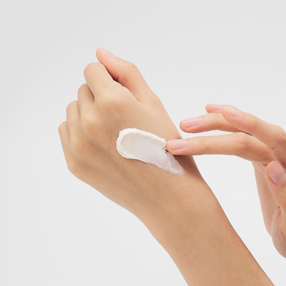 Eine Hand trägt eine weiße Creme auf den Unterarm auf.