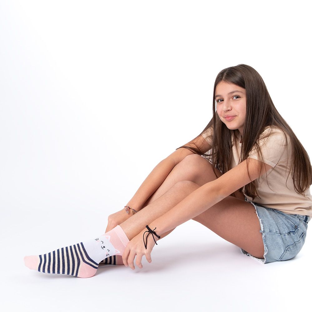 Mädchen sitzt, trägt Socken mit Katze und Streifen. Rosa Zehen und Fersen. Hellrosa und marineblaue Streifen.