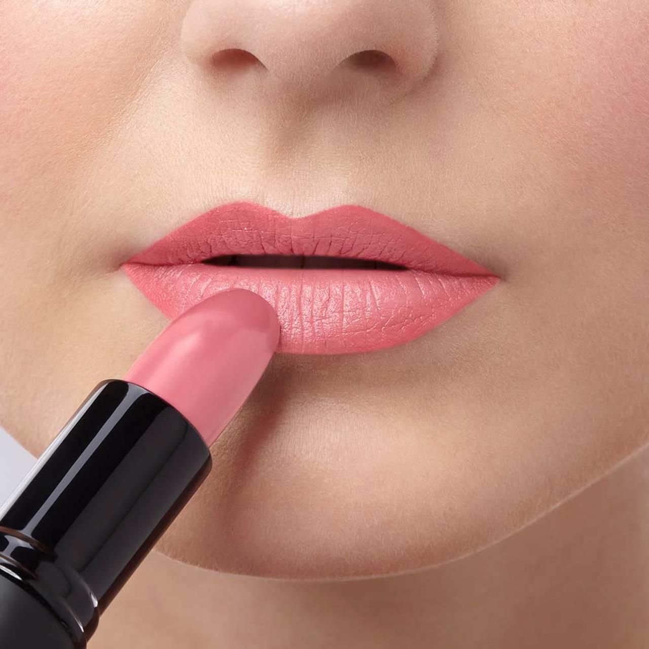 Person trägt rosafarbenen Lippenstift auf den Lippen auf. Nahaufnahme.