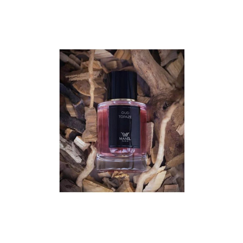 Parfumflakon mit schwarzem Deckel und Etikett. Aufschrift: Oud Topaze, Manel Paris. Auf Holzstücken platziert.