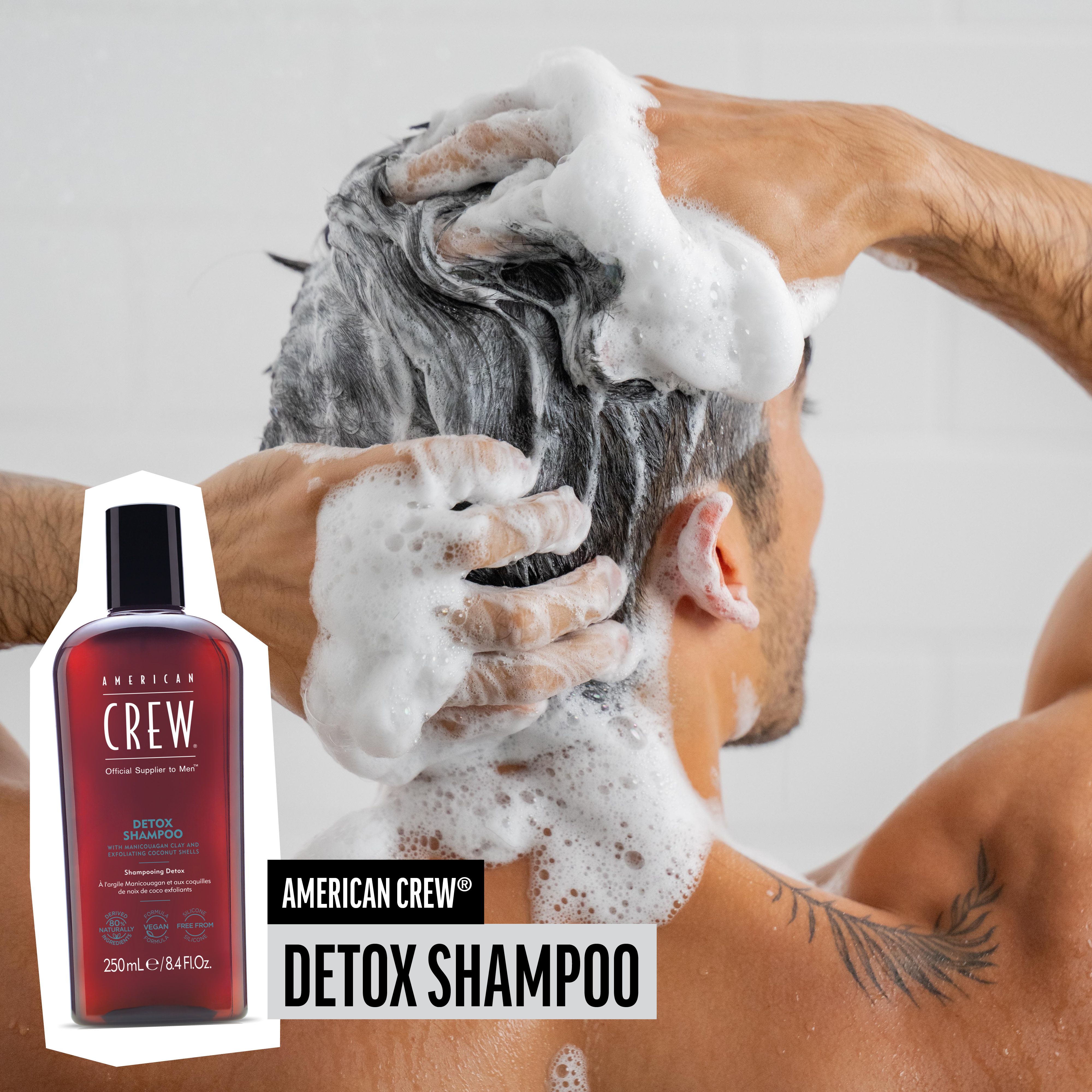 Mann wäscht sich die Haare mit Schaum. AMERICAN CREW Detox Shampoo-Flasche daneben.