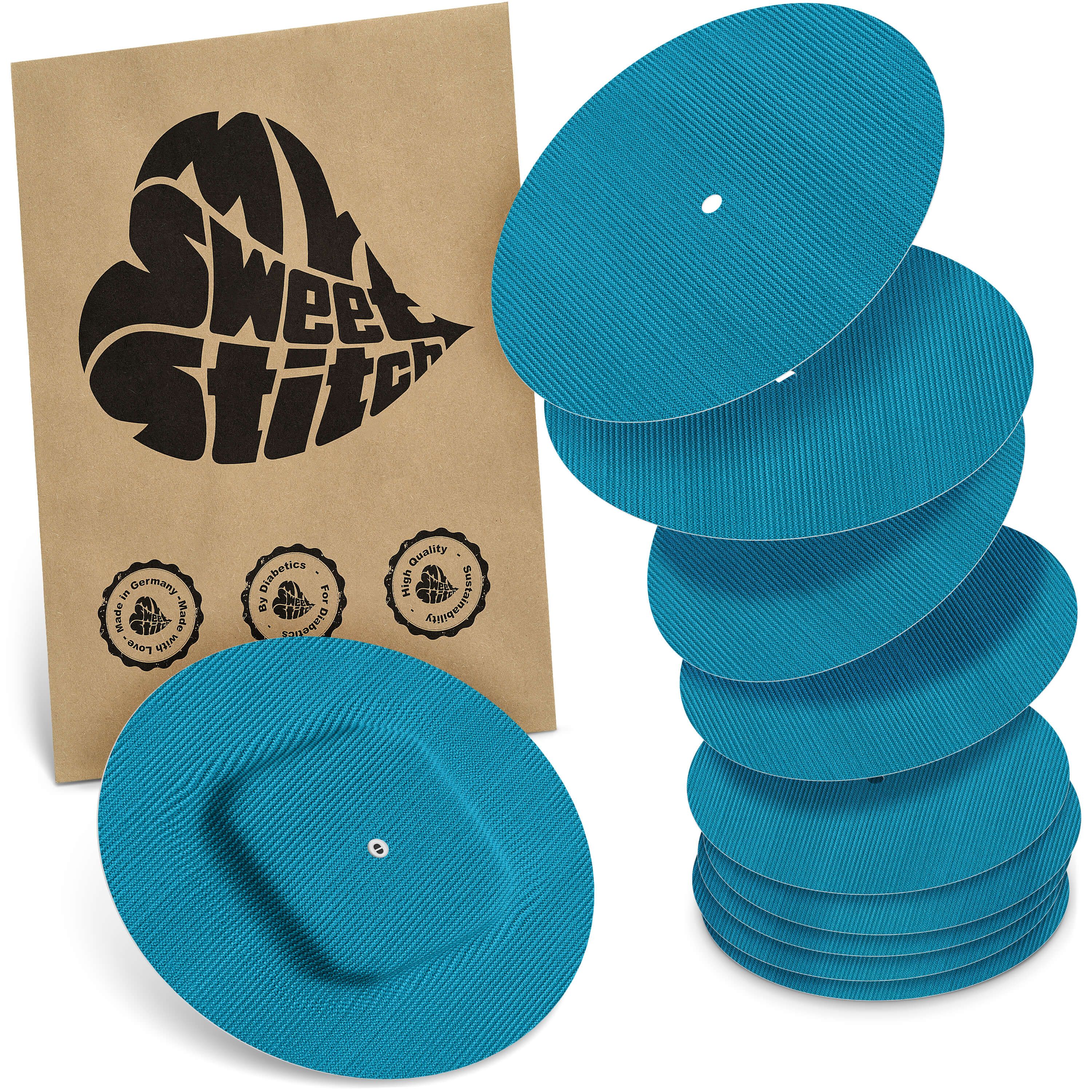 Türkisfarbene, runde Pflaster mit geriffelter Oberfläche. Einige sind gestapelt, eines liegt flach. Braune Verpackung mit Logo.