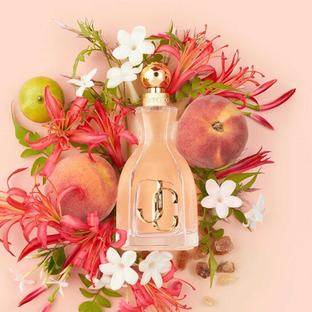 Parfümflakon umgeben von Blüten und Früchten. Rosa Flüssigkeit im Flakon. Goldfarbenes Logo.