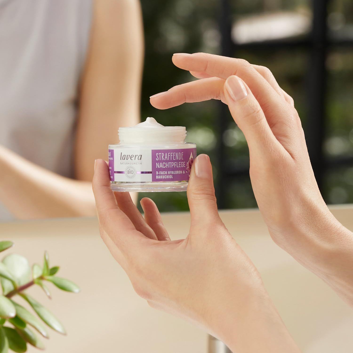 Hände halten einen Tiegel Creme. Auf dem Etikett: Straffende Nachtpflege, 3-fach Hyaluron & Bakuchiol. Marke: lavera.