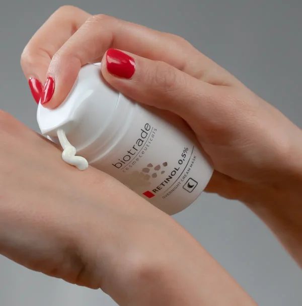 Weiße Flasche mit Aufschrift Biotrade, Retinol 0,5%. Creme wird auf Hand aufgetragen. Nachtcreme-Gesichtsmaske.